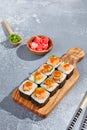 Maki roll with salmon tartare top and tobiko on wooden board in contemporary composition. Sushi roll with chopsticks on concrete