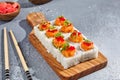 Maki roll with salmon and tobiko caviar on wooden board in contemporary composition. Sushi roll with chopsticks on concrete table