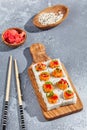 Maki roll with salmon and tobiko caviar on wooden board in contemporary composition. Sushi roll with chopsticks on concrete table