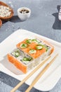 Maki roll with salmon and wasabi sauce on white plate in contemporary composition. Sushi roll with chopsticks on concrete table.