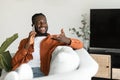 Making call. Happy african american man talking on smartphone and gesturing, resting on sofa at home, free space Royalty Free Stock Photo