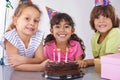 Making childhood memories. Three friends at a birthday party smiling with a cake in front of them. Royalty Free Stock Photo