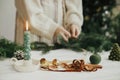 Making Christmas modern wreath. Stylish candle as fir tree, golden bells and ribbon on background of woman hands making boho