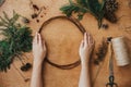 Making christmas wreath. Hands holding wooden circle and fir branches, pine cones, thread, scissors, herbs on wooden table. Royalty Free Stock Photo