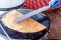 Making crepes pancakes at a food market. A hand is making crepes outdoors on a metal griddle