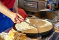Making crepes pancakes at a market. A hand makes crepes on a metal grill with a stick