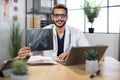 Male Asian Indian doctor, sitting in office, holding skull xray image, working on laptop