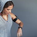 Making great progress. a sporty young woman checking the time on her sports watch against a gray background. Royalty Free Stock Photo