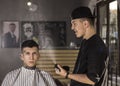 Young man is prepared to get haircut by happy barber while sitting in chair at barbershop