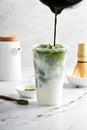 Making iced matcha latte in a tall glass with ice by adding matcha tea to milk Royalty Free Stock Photo