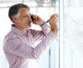 Making important business decisions. A mature businessman talking on his cellphone while writing something on a glass Royalty Free Stock Photo