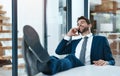 Making millions with one phone call. a handsome young businessman relaxing with his feet up on an office desk while Royalty Free Stock Photo