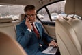Making money. Confident and stylish mature businessman in full suit working on his laptop and talking on the phone with Royalty Free Stock Photo