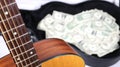 Acoustic guitar corner and neck up close in focus, money in case out of focus, strong depth of field