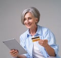 Making online payment mature woman 50s hold credit, debit card and digital tablet working or shopping online. Pretty Royalty Free Stock Photo