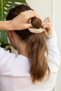 Making ponytail with beige scrunchie with long natural blond hair. Caucasian young woman with gold glasses view from the back. Royalty Free Stock Photo