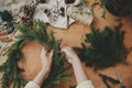 Making rustic Christmas wreath flat lay. Hands holding fir branches, and pine cones, thread, berries, scissors on wooden table. Royalty Free Stock Photo