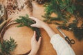 Making rustic christmas wreath flat lay. Hands holding fir branches and pine cones, thread, scissors on wooden table. Details for Royalty Free Stock Photo