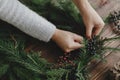 Making rustic christmas wreath, seasonal winter workshop. Florist holding berries on wooden table