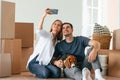 Making selfie. Young couple with dog are moving to new home