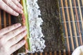 Making Sushi Rolls at Home: Female Hands Roll Nori Seaweed Sheet on a Bamboo Mat. Ingredients: Salmon Fish Strips, Cucumber Royalty Free Stock Photo