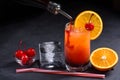 Making Tequila Sunrise Cocktail. Grenadine slowly poured into a glass of ice, orange juice and tequila. Dark stone background with Royalty Free Stock Photo