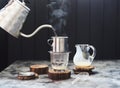 Making Vietnamese coffee with condensed milk. Pouring hot water from goose neck kettle into glass through phin on dark background Royalty Free Stock Photo
