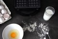 Making waffles at home - a glass of milk, a waffle maker, a broken egg in a bowl, flour and a whisk for mixing. cooking Viennese
