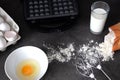 Making waffles at home - a glass of milk, a waffle maker, a broken egg in a bowl, flour and a whisk for mixing. cooking Viennese