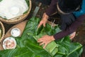 Making wrapping Chung Cake, the Vietnamese lunar new year Tet food outdoor with old woman hands and ingredients. Closed-up.