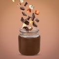 Making yummy chocolate paste. Hazelnuts and pieces of chocolate falling into jar on light brown background Royalty Free Stock Photo