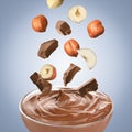 Making chocolate paste. Hazelnuts and pieces of chocolate falling into bowl on light blue background Royalty Free Stock Photo