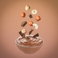 Making yummy chocolate paste. Hazelnuts and pieces of chocolate falling into bowl on light brown background Royalty Free Stock Photo