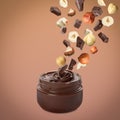 Making yummy chocolate paste. Hazelnuts and pieces of chocolate falling into jar on light brown background Royalty Free Stock Photo