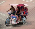 Malacca, Malaysia--February 2018: A couple of tourists ride a colorful trishaw along the brick-paved Dutch Square in Melaka,