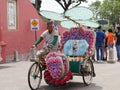 Malacca, Malaysia--February 2018: Wide shot of a man driving a colorful trishaw along the brick-paved Dutch Square in Melaka,