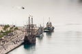 Pier one in the port of Malaga, Spain where is the lighthouse known as `La Farola` and several docked ships, including a galleon a