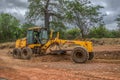 Full view of a road grader machine, leveling the ground with person to drive