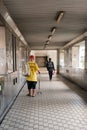 Malaysia - July 27 2023: Elderly in Yellow With a Walking Cane Crossing Sheltered Bridge