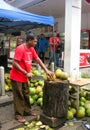 Malaysian man cutting young coconuts