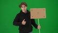 A male activist holds a blank poster and shows a thumbs up. A young man in casual clothes holds a placard on a green Royalty Free Stock Photo