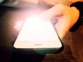 Male adult`s hand holds white personal smartphone with brightness and flare on the screen