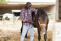 Male african american farmer removes saddle from horse at stable