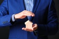 Male agent covering wooden house on black background, closeup.