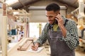 Male Apprentice Working As Carpenter In Furniture Workshop Making Phone Call Royalty Free Stock Photo