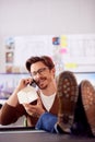 Male Architect In Office With Feet On Desk Taking Call On Mobile Phone And Looking At Wooden Model