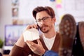 Male Architect In Office With Feet On Desk Taking Call On Mobile Phone And Looking At Wooden Model