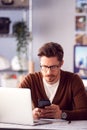 Male Architect In Office With Laptop Working On Plan At Desk Text Messaging On Mobile Phone Royalty Free Stock Photo