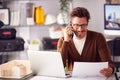 Male Architect In Office Working At Desk On Laptop Taking Call On Mobile Phone Royalty Free Stock Photo