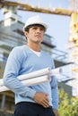 Male architect with rolled up blueprints standing at construction site Royalty Free Stock Photo